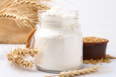 Cam kavanozda buğday unu, beyaz masada tahıl ve çiviler, yakın plan.