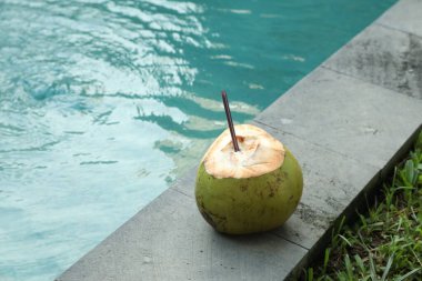 Yeşil hindistan cevizi, ferahlatıcı bir içecek ve açık havuzun yanında saman.