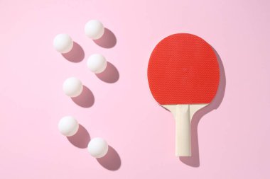 Masa tenisi raketi ve toplar pembe arka planda, düz yatıyordu.