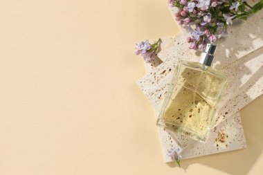 Bir şişe parfüm ve soluk sarı arka planda güzel leylak çiçekleri. Metin için boşluk