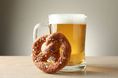 Lezzetli kraker ve bir bardak bira ahşap masada, gri arka planda, yakın planda.