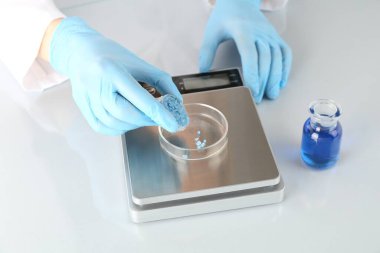 Bilim adamı beyaz ayna masasındaki terazide numune tartıyor, yakın plan.