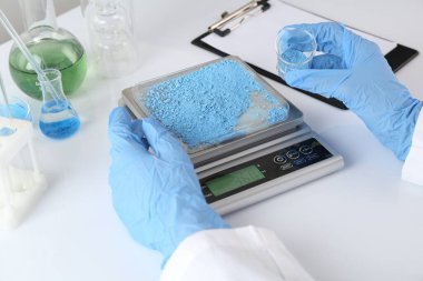 Bilim adamı beyaz masadaki terazide numune tartıyor, yakın plan.