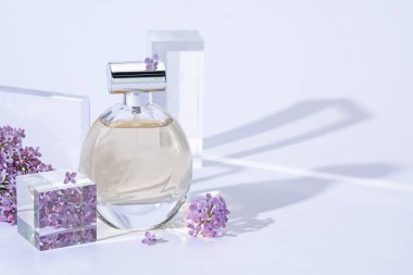 Açık gri arka planda parfüm şişesi ve leylak çiçeklerinin şık sunumu, yakın plan. Metin için boşluk