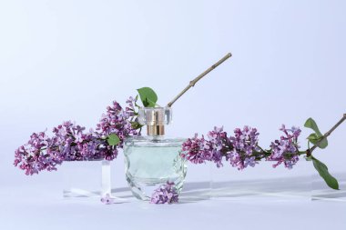 Parfüm şişesi ve açık gri arka planda leylak çiçekli dallar, yakın plan.