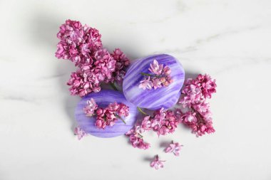 Beyaz mermer masanın üstünde sabun çubukları ve leylak çiçekleri var.