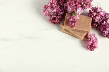 Beyaz mermer masanın üstünde sabun ve leylak çiçekleri yığını var. Metin için boşluk