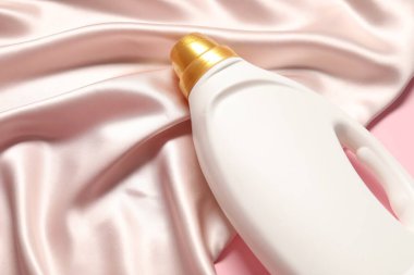 Bir şişe yumuşatıcı ve pembe arka planda bej kumaş.