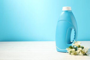 Beyaz ahşap masada açık mavi arka planda bir şişe yumuşatıcı ve zambak çiçeği. Metin için boşluk