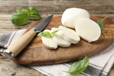 Ahşap masada fesleğen ve bıçakla mozzarella peyniri kes, yakın plan.