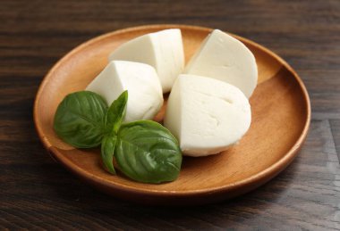 Ahşap masada lezzetli mozzarella peyniri ve fesleğen parçaları, yakın plan.