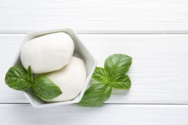 Lezzetli mozzarella peyniri ve fesleğen parçaları beyaz ahşap masada, düz yerde. Metin için boşluk