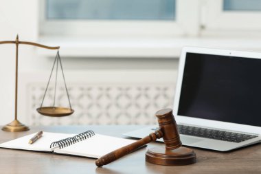 Dizüstü bilgisayar, yargıç tokmağı ve terazileri ofisteki ahşap masada.