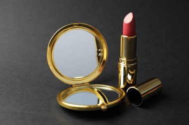 Siyah arkaplanda cep aynası ve ruj, yakın plan.