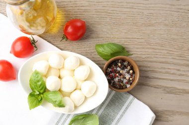 Lezzetli mozarella peyniri topları, domatesler, fesleğen, yağ ve biberler ahşap masada, düz yatak. Metin için boşluk