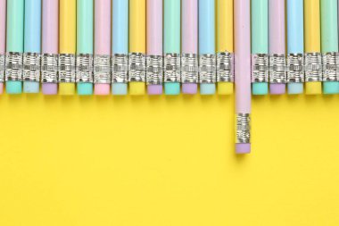 Sarı arka planda silgisi olan bir sürü grafit kalem, düz bir zemin. Metin için boşluk