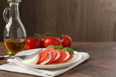 Lezzetli mozzarella, domates, yağ ve fesleğen ahşap masada, yakın plan.