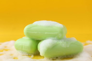 Sarı arka planda köpüklü sabun çubukları, yakın plan.