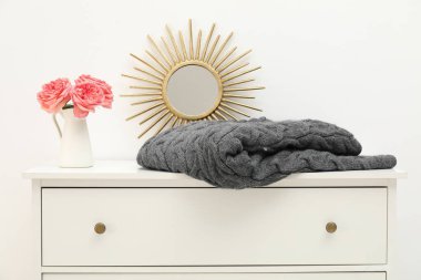 Gri yün battaniye, ayna ve vazodaki güzel çiçekler kapalı alandaki beyaz çekmecede.