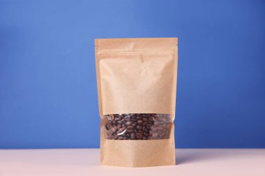 Mavi arka planda beyaz masada kahve çekirdekleri olan fermuarlı bir stand-up kesesi. Tasarım için model