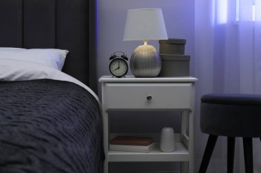 İçinde lamba, çalar saat ve yatağın yanındaki dekorun bulunduğu komodin.