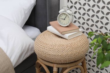 Çalar saati olan yan masa ve yatağın yanında kitaplar.