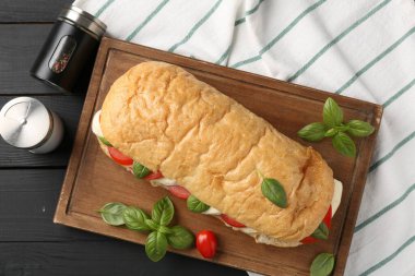 Mozarella peynirli, domatesli, fesleğenli ve baharatlı lezzetli sandviç siyah ahşap masada, düz yatıyordu.