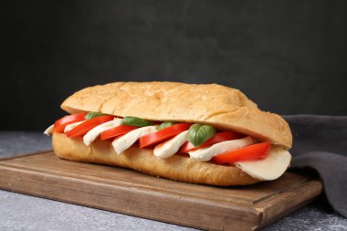 Mozarella peynirli, domatesli ve fesleğenli lezzetli sandviç. Gri desenli masa, koyu arkaplanlı, yakın plan.