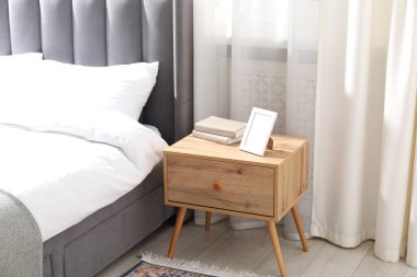 Yatağın yanında kitap ve çerçeve olan komodin.