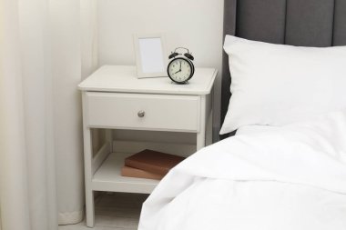 Alarm saati ve yatağın yanındaki çerçeveli komodinin yanında.