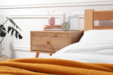 Yatağın yanında çalar saati, kitapları ve dekorasyonu olan bir komodin.