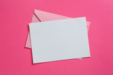 Pembe arka planda boş davetiye ve zarf, üst manzara. Tasarım için boşluk