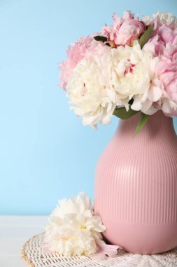 Beyaz masadaki vazodaki güzel şakayıklar açık mavi duvarın yanında, yakın plan.