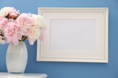 Vazodaki güzel şakayıklar ve resim çerçevesi açık mavi duvarın yanındaki beyaz masada.