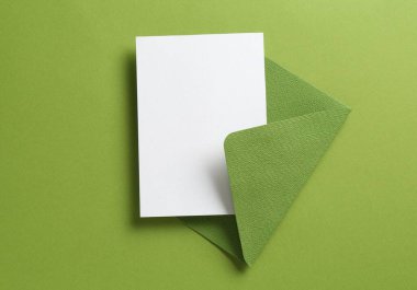 Yeşil arka planda boş davetiye ve zarf, üst manzara. Tasarım için boşluk