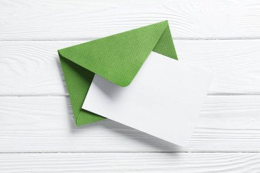 Beyaz ahşap masa üzerinde boş davetiye ve zarf, üst manzara. Tasarım için boşluk