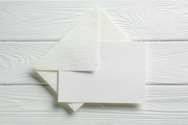 Beyaz ahşap masa üzerinde boş davetiye ve zarf, üst manzara. Tasarım için boşluk