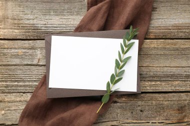 Boş davetiye kartı, zarf ve yeşil dal, ahşap masa, üst manzara.
