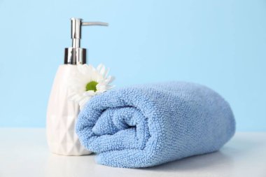 Yumuşak havlu, sıvı sabun ve kasımpatı çiçeği açık mavi arkaplanda, yakın plan.