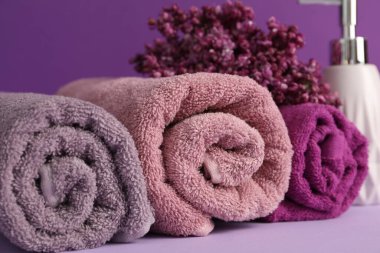 Yumuşak havlular, sıvı sabun ve mor arka planda leylak çiçekleri, yakın plan.