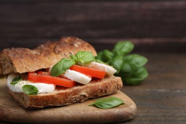 Mozarella peynirli, domatesli ve ahşap masadaki fesleğenli lezzetli sandviç, yakın plan. Metin için boşluk
