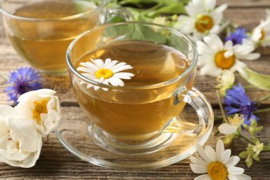 Cam bardaklarda romatik bitki çayı ve ahşap masada çiçekler, yakın plan.