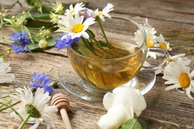 Cam bardakta Aromatik bitki çayı, tahta masada çiçekler ve kepçe, yakın plan.