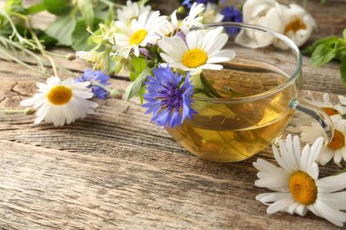 Cam bardakta Aromatik bitki çayı ve ahşap masada çiçekler, yakın plan. Metin için boşluk
