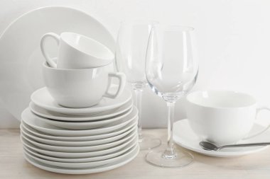 Beyaz duvarın yanındaki açık ahşap masada farklı temiz bulaşık takımı.