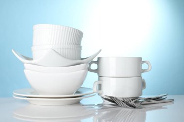 Açık mavi arkaplana karşı beyaz masada farklı temiz bulaşık takımı