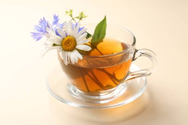 Cam fincanda aromatik bitki çayı ve bej arka planda farklı çiçekler, yakın plan.
