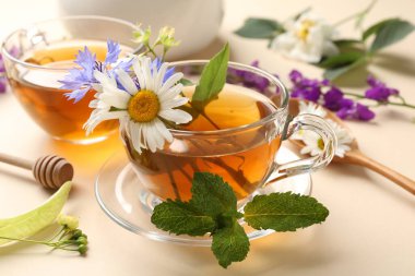 Cam fincanlarda aromatik bitki çayı, farklı çiçekler ve bej arka planda nane şekeri, yakın plan.