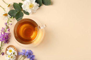 Cam fincanda aromatik bitki çayı ve bej arka planda farklı çiçekler. Metin için boşluk