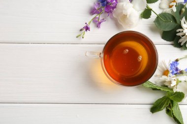 Cam fincanda aromatik bitki çayı, farklı çiçekler ve beyaz ahşap masada nane şekeri. Metin için boşluk